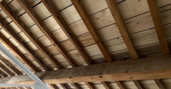 Plafond avec poutres en bois, supports en métal blanc.